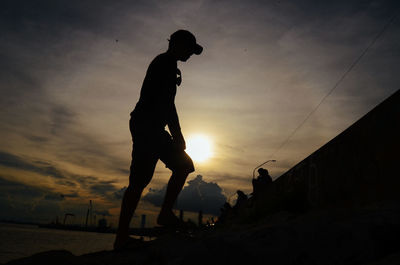 Silhouette man standing by sea against sky during sunset