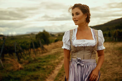 Young woman looking away while standing on field against sky