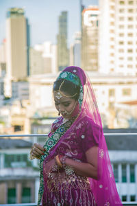 Asian woman wearing a traditional saree touching her cloth with urban building background.