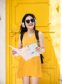 Young woman wearing sunglasses standing against yellow door