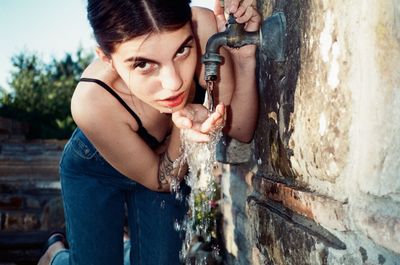 Portrait of young woman drinking water from faucet