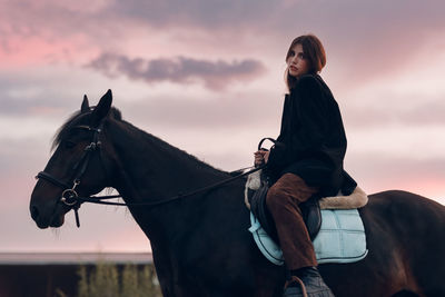 Side view of man riding horse against sky