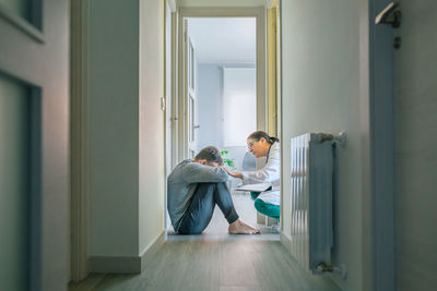 Doctor reassuring and helping to patient sitting on room floor