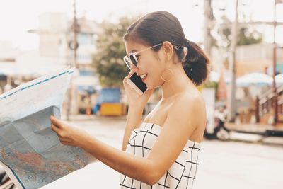 Side view of smiling mid adult woman with world map using phone on street