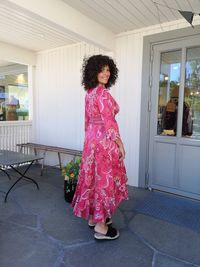 Portrait of mature woman in pink dress standing against house