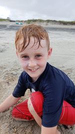 Portrait of smiling wet boy playing on sand at beach