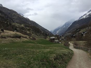 Dirt road on field by mountains against sky