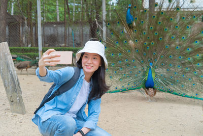 Smiling woman doing selfie with peacock