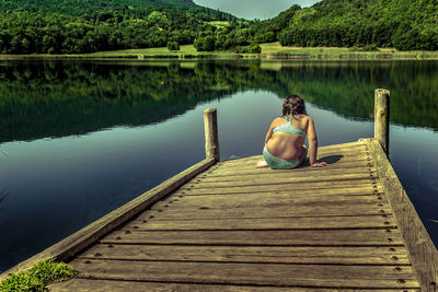 Rear view of woman sitting on pier over lake