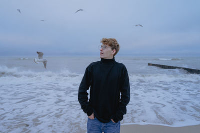 Seagulls are flying, a young man in a sulfur walk stands on the shore of a stormy sea with an 