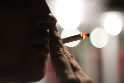 Close-up of young woman holding cigarette against blurred background