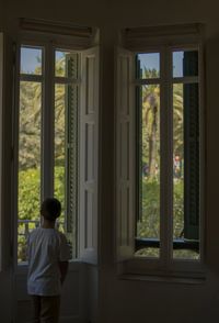Rear view of boy looking through window