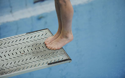 Low section of person standing on diving platform over swimming pool