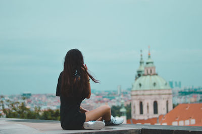 Woman sitting against sky in city
