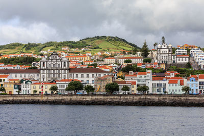 Town by river and buildings in city against sky