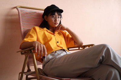 Portrait of young woman sitting on chair against wall