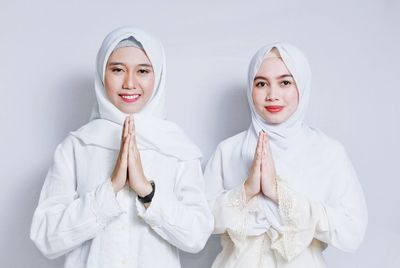 Portrait of smiling women wearing hijabs greeting against white background