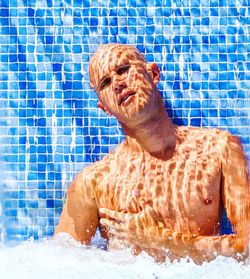 Portrait of shirtless shaved head man against blue tile wall in swimming pool