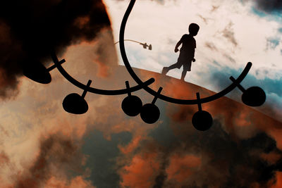 Silhouette boy playing with ball against sky during sunset