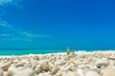 Surface level view of mother and son standing at beach against blue sky