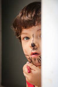 Close-up portrait of boy with face paint hiding behind wall