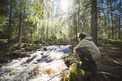 Woman crouching next to stream in forest