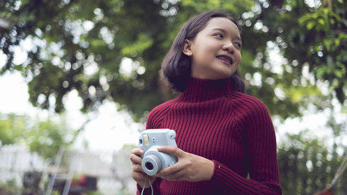 Asian girl hold blue camera with happy emotion and nature background.