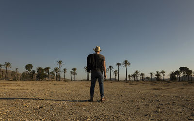 Adult man in cowboy hat on tabernas desert with palm trees against blue sky. almeria, spain
