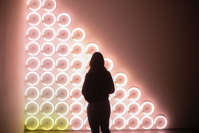 Rear view of silhouette woman standing against illuminated lights