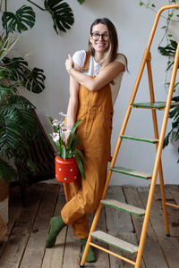 Young happy woman gardener standing near stepladder in home garden with tropical house plants