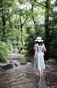 Rear view of woman standing in river at forest