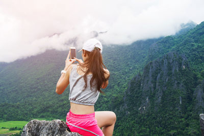 Rear view of woman standing on cliff against mountains