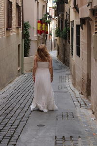 Rear view of woman walking on footpath amidst buildings