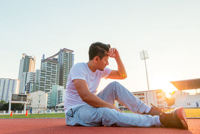 Full length of man sitting on track against buildings and sky