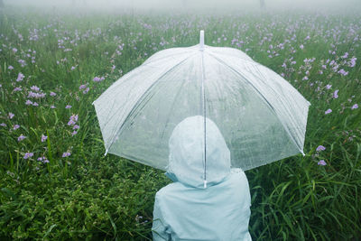 Rear view of woman with umbrella standing on field during rainy season