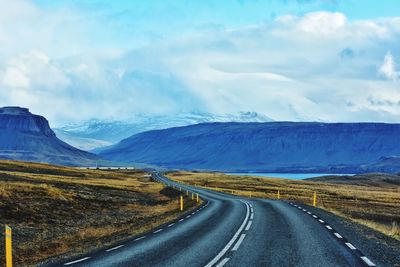 Diminishing perspective of road leading towards mountains against cloudy sky