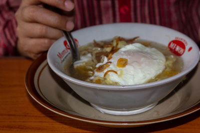 Close-up of hand holding soup in bowl on table