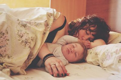 Mother with son sleeping on bed at home