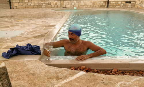 Man swimming in pool and drinking white wine 