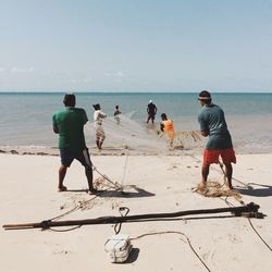 Fishermen pulling fishing net on shore against sky