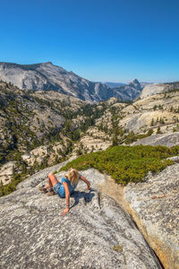 Full length of person on rock in mountains against blue sky