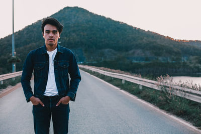 Portrait of young man standing on road against sky