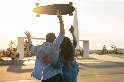 Stylish young couple hug looking at sunset hold skateboard. happy girl and guy in love enjoy freedom