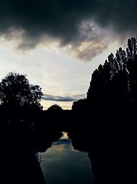 Reflection of silhouette trees on water against sky