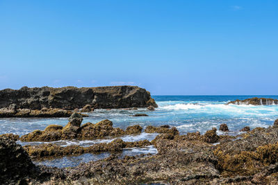 Scenic view of rocks on beach against clear blue sky