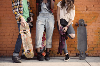 Low section of friends standing by brick wall with skateboards