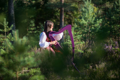 Woman playing harp against trees in forest