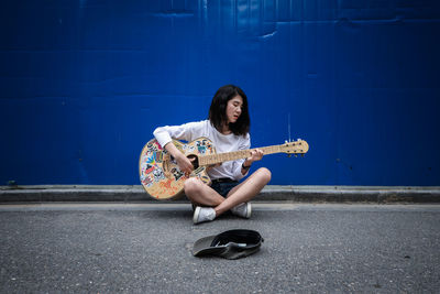 Woman playing guitar against blue wall