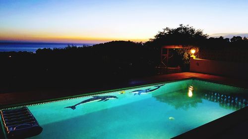 Swimming pool by sea against sky at sunset