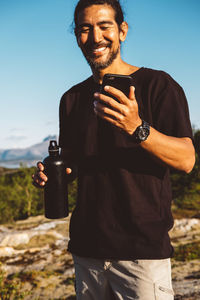 Man smiling holding his phone and a water bottle in a sunny day